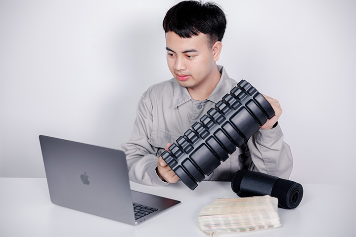 a male worker in front of a computer is holding a foam roller